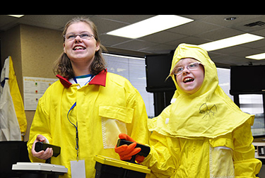 Image of two your girls in yellow protective coats holding remote controls.